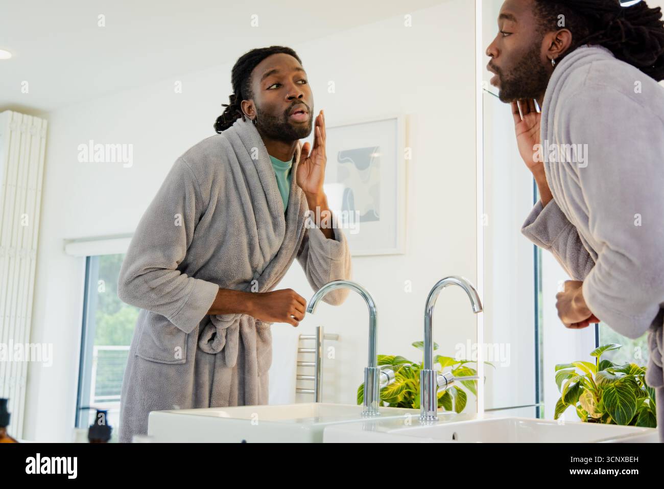 Uomo afroamericano che studia la mandibola nello specchio di casa con doppio lavandino con rubinetti cromati Foto Stock