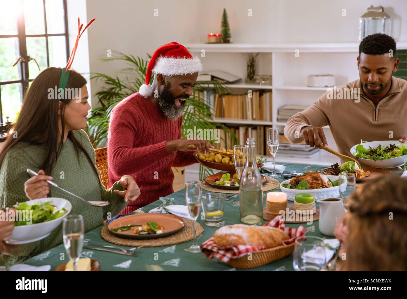 Diversi amici nel cappello di babbo natale, fascia di renna seduta a casa a condividere il pasto con un panno holly Foto Stock