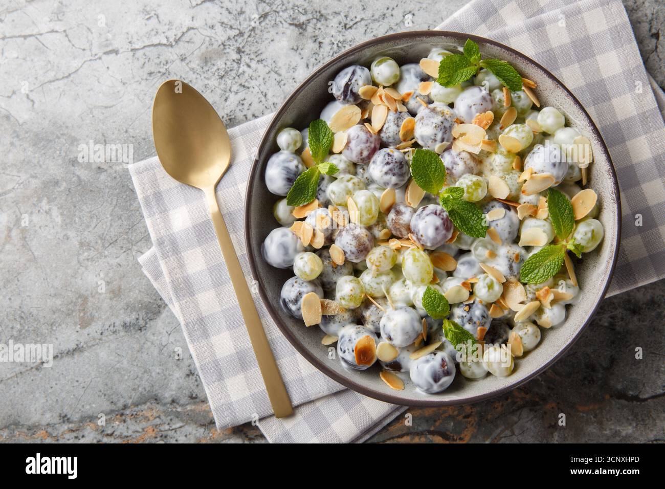 Insalata fresca di uva Sultana dolce con scaglie di mandorle, menta, yogurt greco e condimento di formaggio spalmabile in un piatto sul tavolo. Vista dall'alto orizzontale Foto Stock