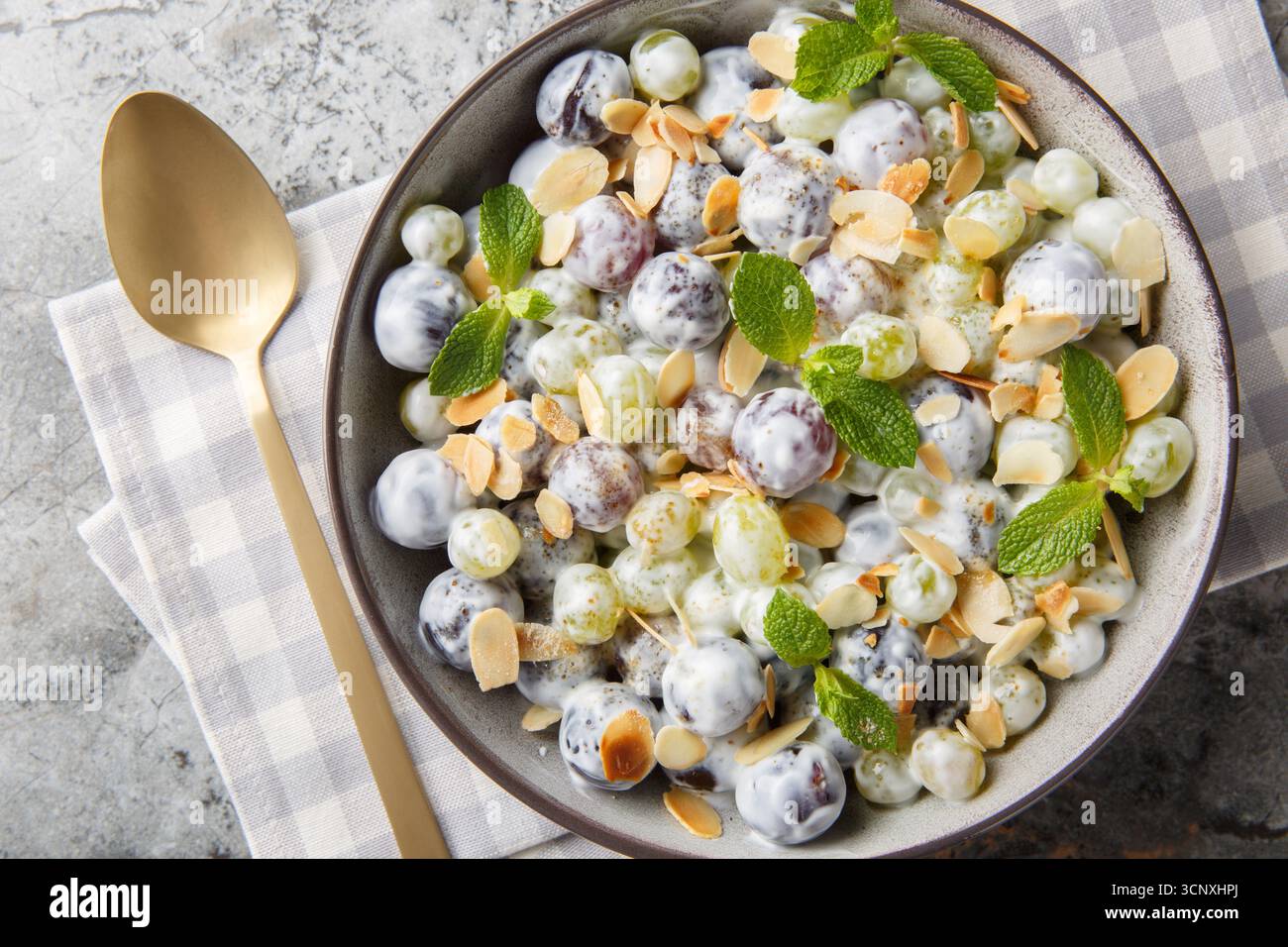 Insalata di uva Sultana con scaglie di mandorle, menta, yogurt greco e condimento di formaggio spalmabile in un piatto sul tavolo. Vista dall'alto orizzontale Foto Stock