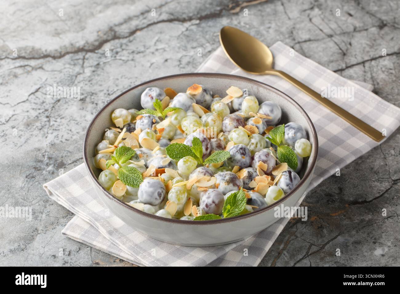 Insalata fresca di uva Sultana dolce con scaglie di mandorle, menta, yogurt greco e condimento di formaggio spalmabile in un piatto sul tavolo. Orizzontale Foto Stock