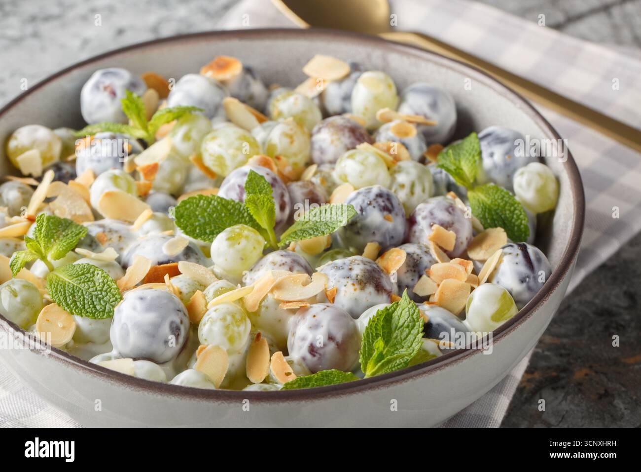 Insalata di uva Sultana con scaglie di mandorle, menta, yogurt greco e condimento di formaggio spalmabile in un piatto sul tavolo. Orizzontale Foto Stock
