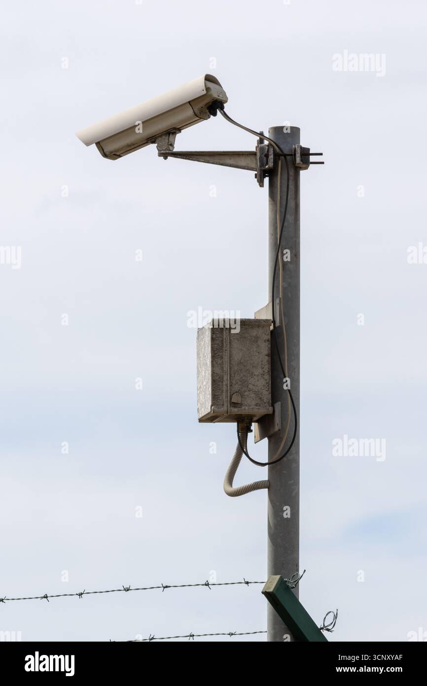 Telecamera di sicurezza che controlla una recinzione di filo spinato, garantendo sicurezza e sorveglianza contro potenziali minacce Foto Stock