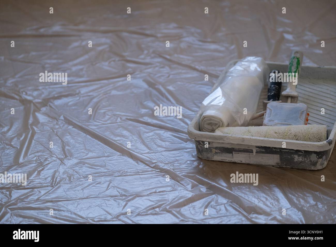 Vassoio per verniciatura con rullo, spazzola e coperchio in plastica posizionati sul pavimento. Concetto di lavori fai da te, progetti di ristrutturazione, servizi di riparazione e costruzione Foto Stock