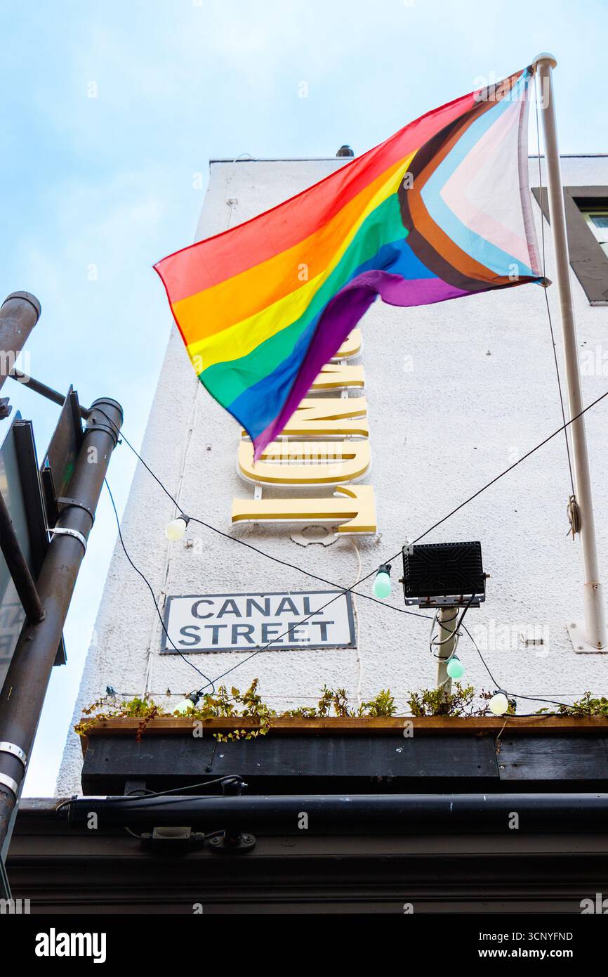 Bandiera dell'orgoglio che sventola fuori da un edificio sul villaggio gay di Canal Street Manchester con sfondo blu del cielo Foto Stock