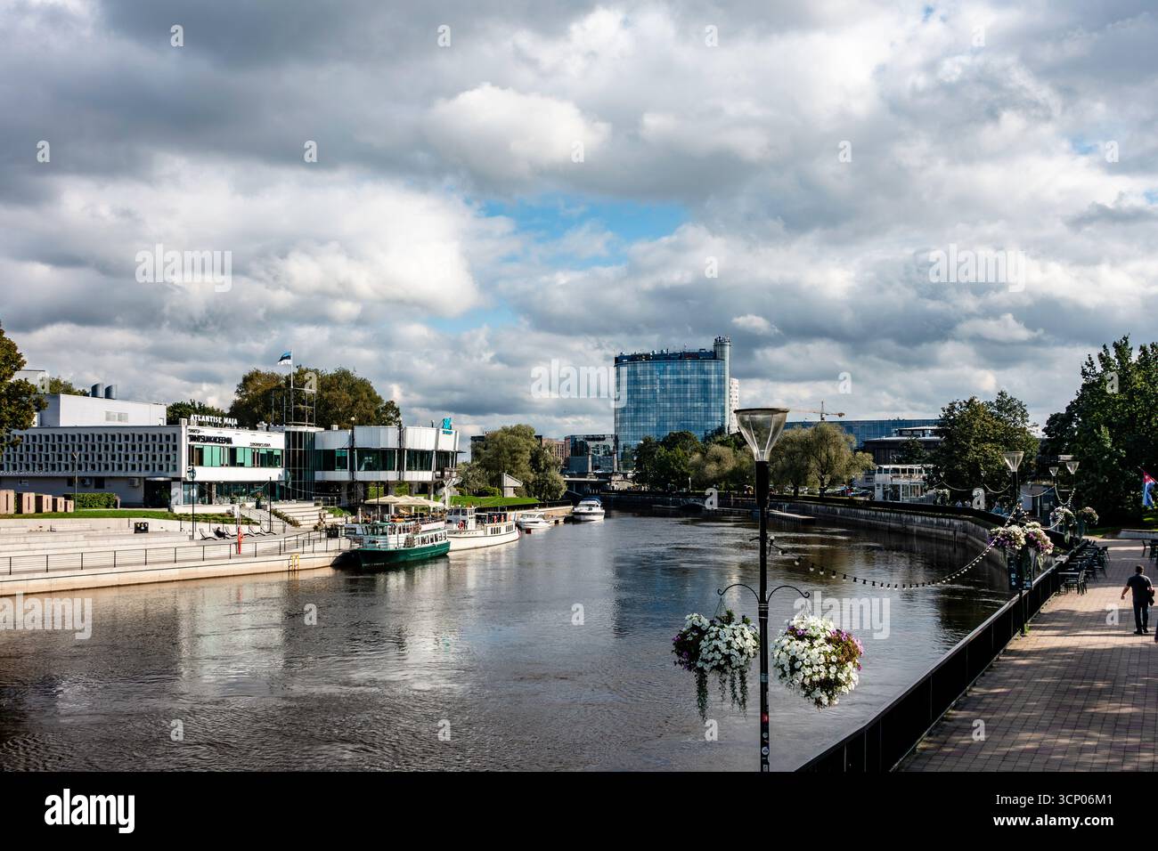 Il fiume Emajõgi a Tartu, in Estonia, con la passeggiata lungo il fiume, le barche e gli edifici moderni sotto cieli nuvolosi, che mostrano il carattere urbano del lungomare della città Foto Stock
