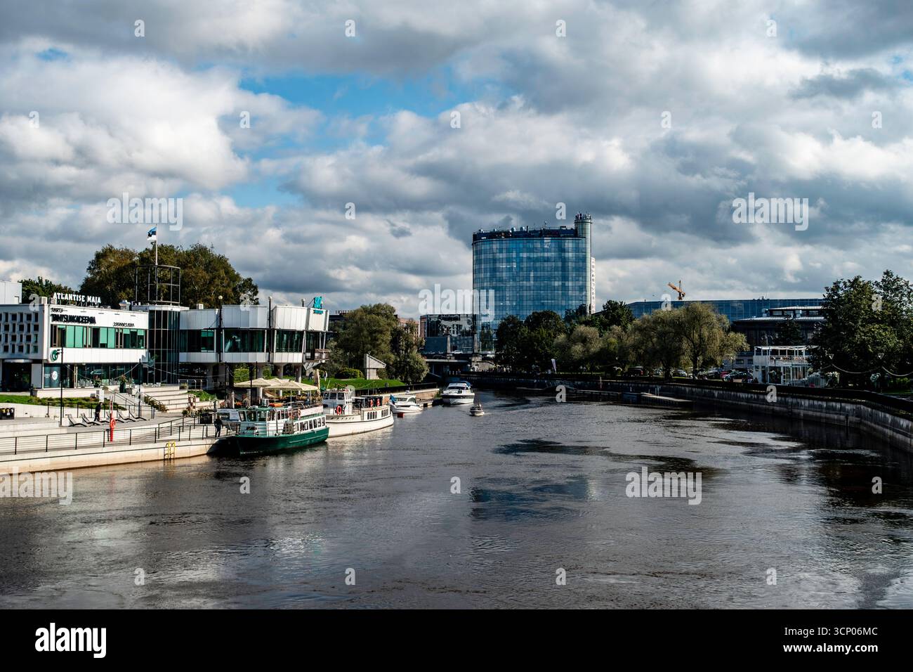 Fiume Emajõgi a Tartu, Estonia, con moderni edifici lungo il fiume, barche e skyline dell'hotel sotto un cielo nuvoloso, che mostra il lungomare urbano della città. Foto Stock