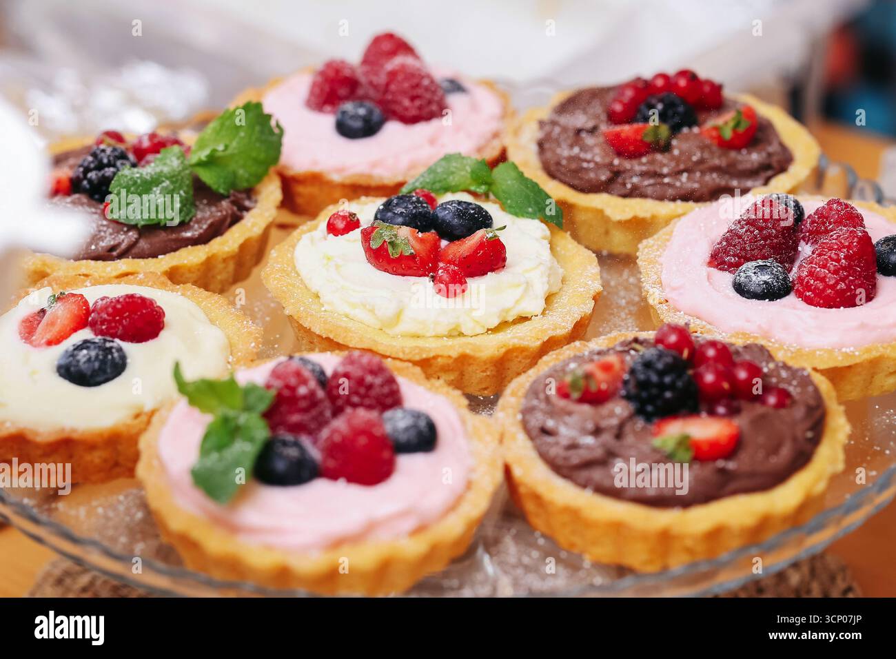 Tortine di frutta dolce con panna e frutti di bosco. Dessert colorato con fragole lampone mirtillo e foglie di menta. Primo piano con pasticcini fatti in casa. Foto Stock