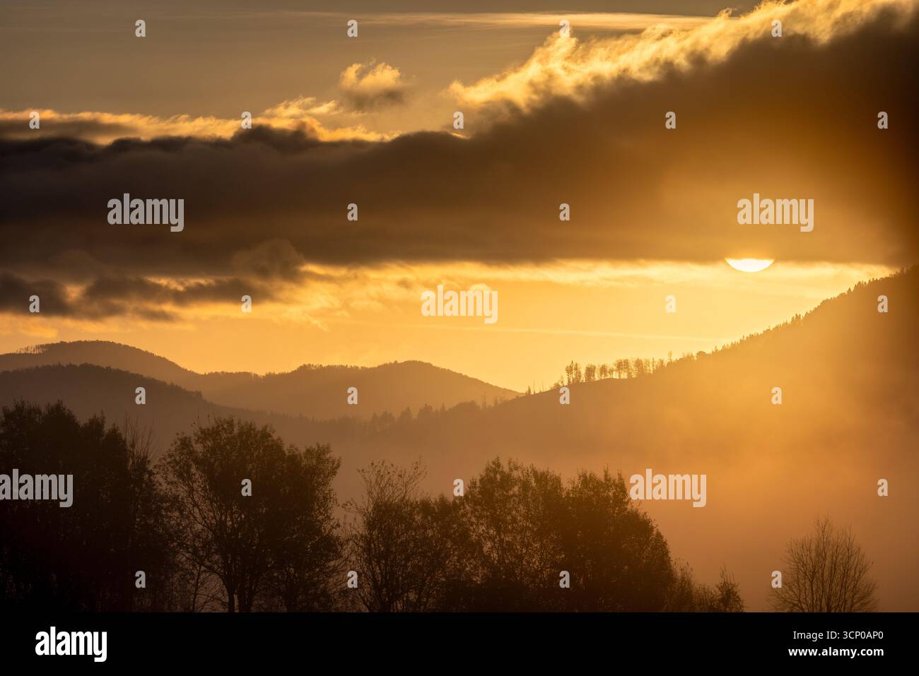 L'ora d'oro bagna il paesaggio montuoso con un bagliore nebbioso mentre il sole si infrangeva tra le nuvole. Foto Stock