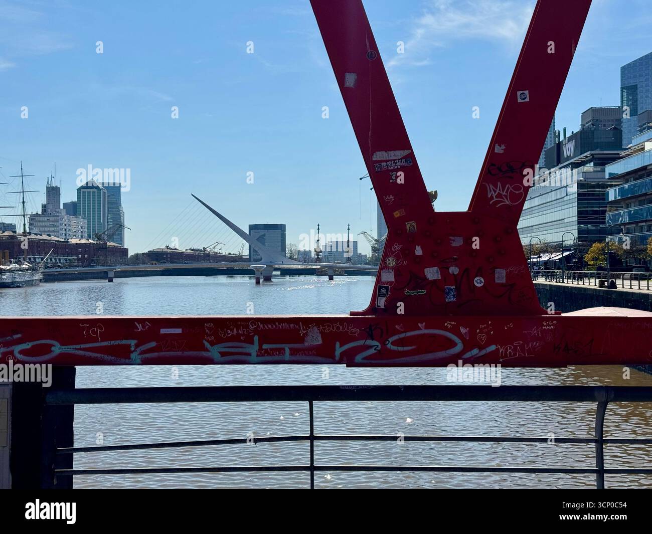 Ponte industriale in acciaio rosso che attraversa un fiume a Buenos Aires, Argentina, con lo skyline della città visibile sullo sfondo sotto un cielo azzurro. - Immagine stock catturata con smartphone