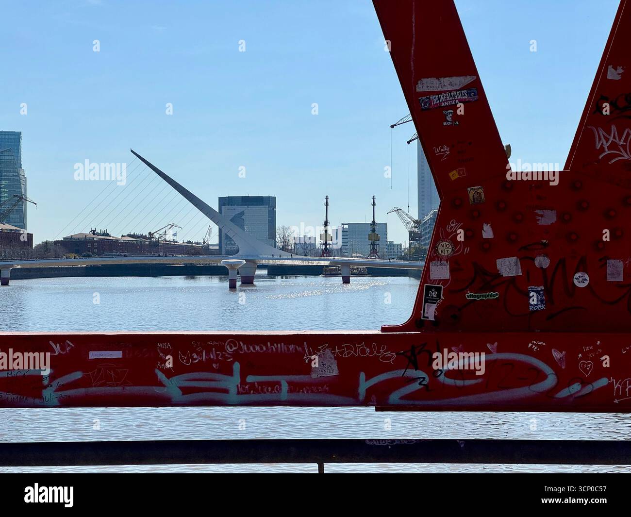 Ponte industriale in acciaio rosso che attraversa un fiume a Buenos Aires, Argentina, con lo skyline della città visibile sullo sfondo sotto un cielo azzurro. - Immagine stock catturata con smartphone