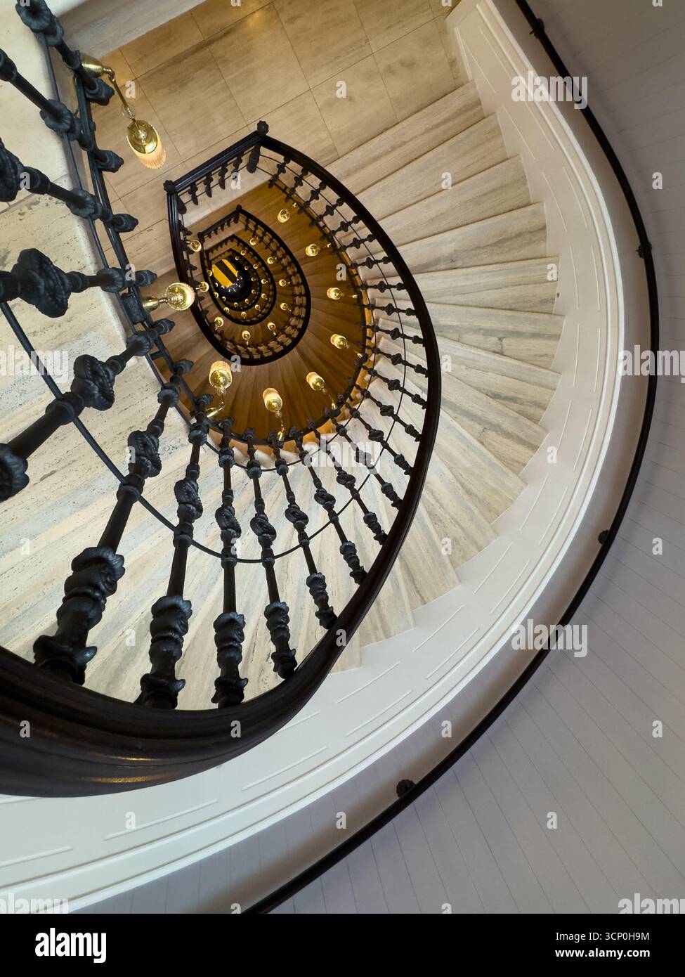 Scala a chiocciola vista dall'alto con balaustra in metallo nero lampadine calde a incandescenza profondità del movimento circolare e dettagli architettonici eleganti che conferiscono un design classico degli interni Foto Stock
