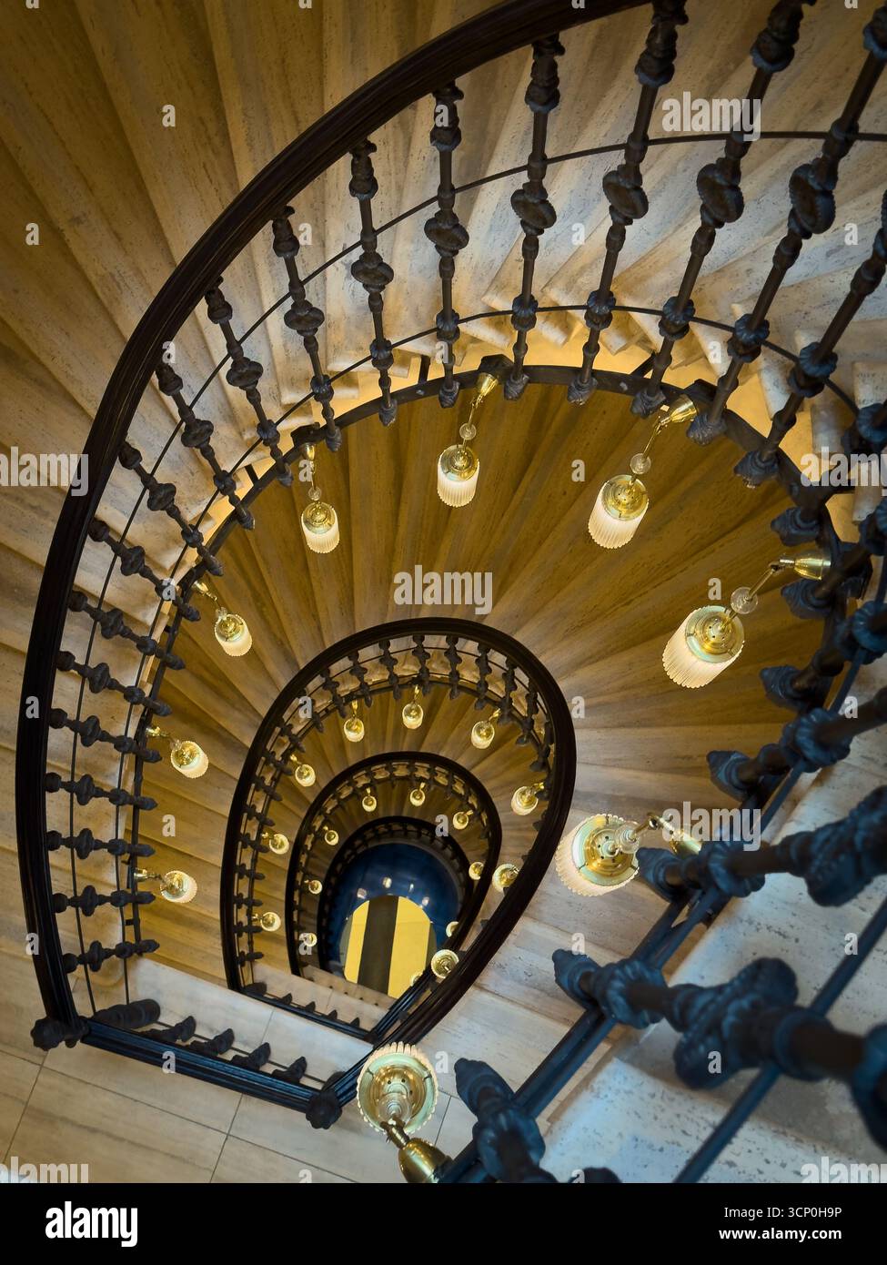 Scala a chiocciola con ringhiera in ferro decorata e lampade a sospensione calde viste dall'alto negli interni storici Foto Stock