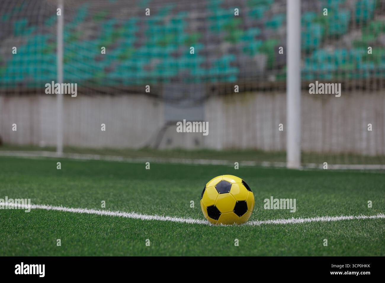 Un vivace pallone da calcio giallo e nero si trova vicino all'angolo di un campo da calcio ben tenuto in uno stadio. Foto Stock