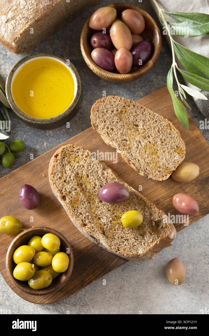 Spuntino mediterraneo con olive miste, olio d'oliva e pane rustico su tavola di legno. Foto Stock