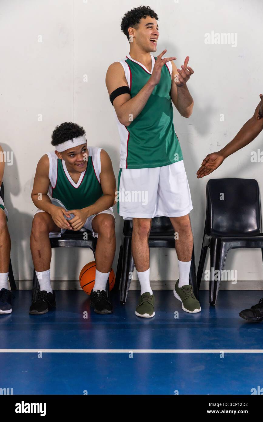 Atleta afroamericana adolescente che indossa una maglia in piedi vicino alla panchina che applaude accanto al basket Foto Stock