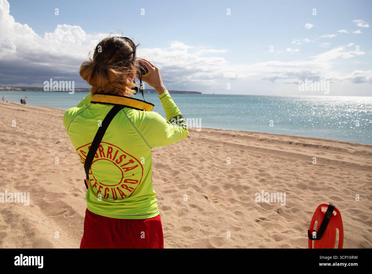 Palma, Spagna. 23 settembre 2025. Un bagnino usa un binocolo mentre pattuglia la spiaggia di Palma, Maiorca. I bagnini delle Isole Baleari si sciopereranno a tempo indeterminato ogni fine settimana da domenica 28 settembre, fino a quando non saranno soddisfatte le loro richieste in merito a condizioni di lavoro precarie e alla mancanza di finanziamenti. Credito: Clara Margais/dpa/Alamy Live News Foto Stock