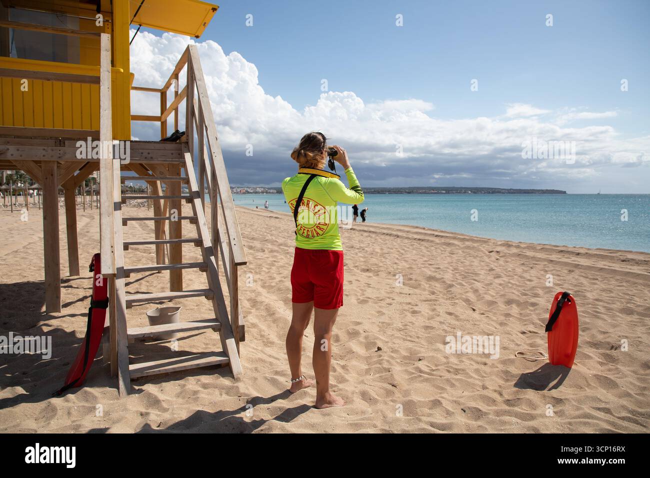 Palma, Spagna. 23 settembre 2025. Un bagnino usa un binocolo mentre pattuglia la spiaggia di Palma, Maiorca. I bagnini delle Isole Baleari si sciopereranno a tempo indeterminato ogni fine settimana da domenica 28 settembre, fino a quando non saranno soddisfatte le loro richieste in merito a condizioni di lavoro precarie e alla mancanza di finanziamenti. Credito: Clara Margais/dpa/Alamy Live News Foto Stock