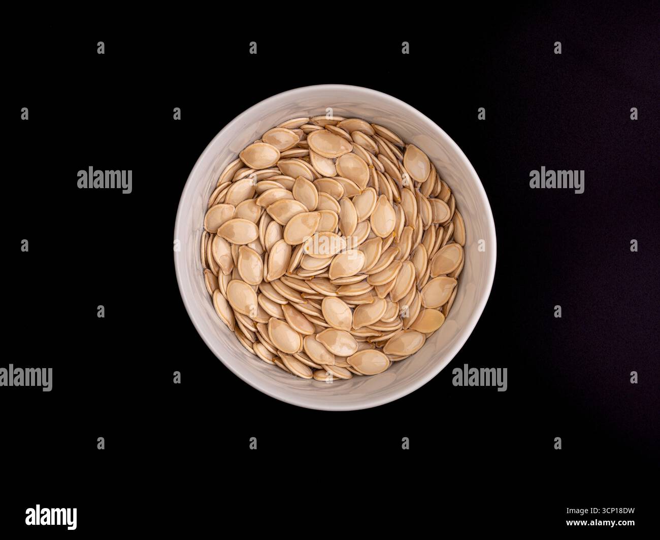 Semi di zucca in un recipiente in ceramica su sfondo nero, ideale per alimenti di stagione. Foto Stock