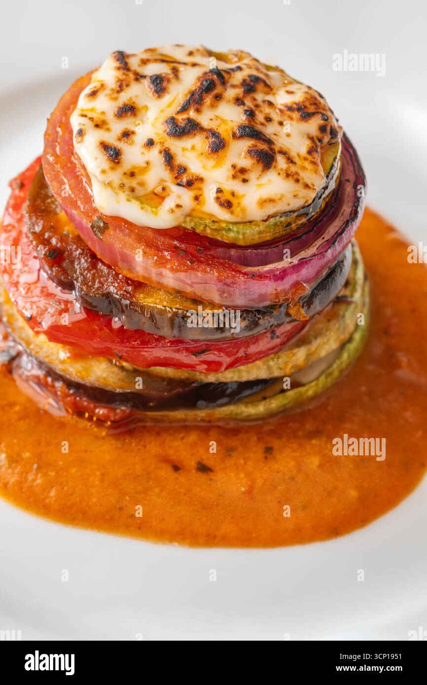 Verdure ratatouille al forno impilate in una torre vibrante, con strati dorati messi in risalto splendidamente Foto Stock
