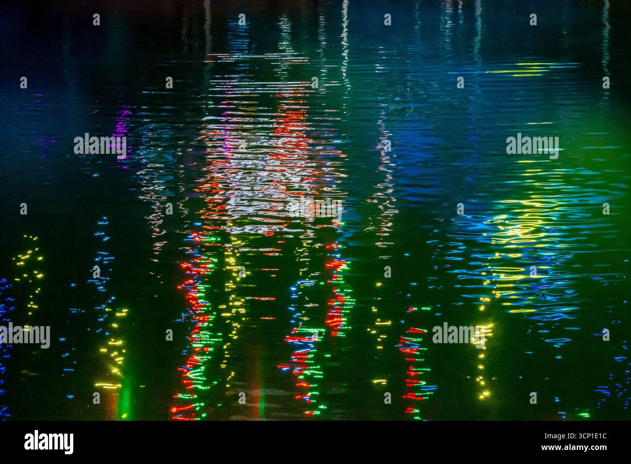 Riflessi colorati al neon sull'acqua notturna: Vivaci luci della città che brillano sulla superficie Foto Stock