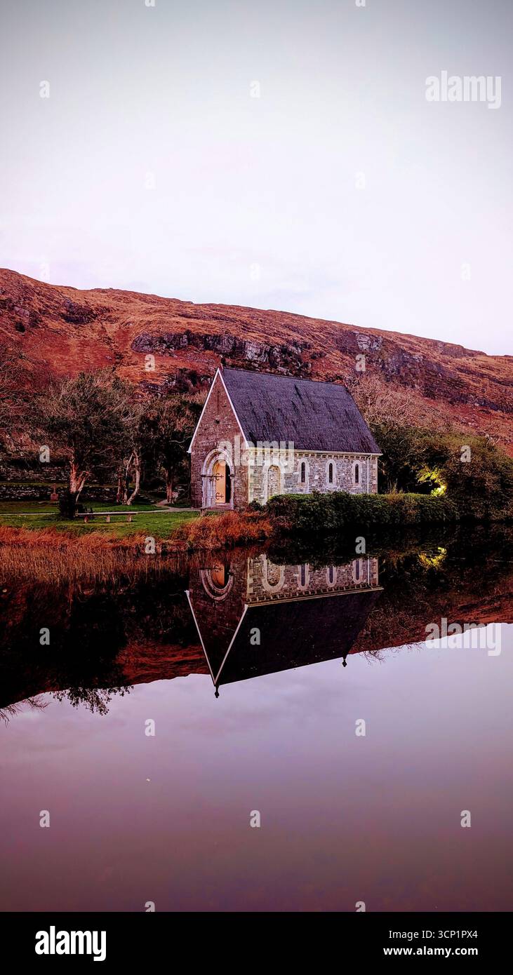 Chiesa di Gougane barra su una piccola isola in un tranquillo lago, circondata da montagne e vegetazione lussureggiante nella contea di Cork, Irlanda. - Immagine stock catturata con smartphone
