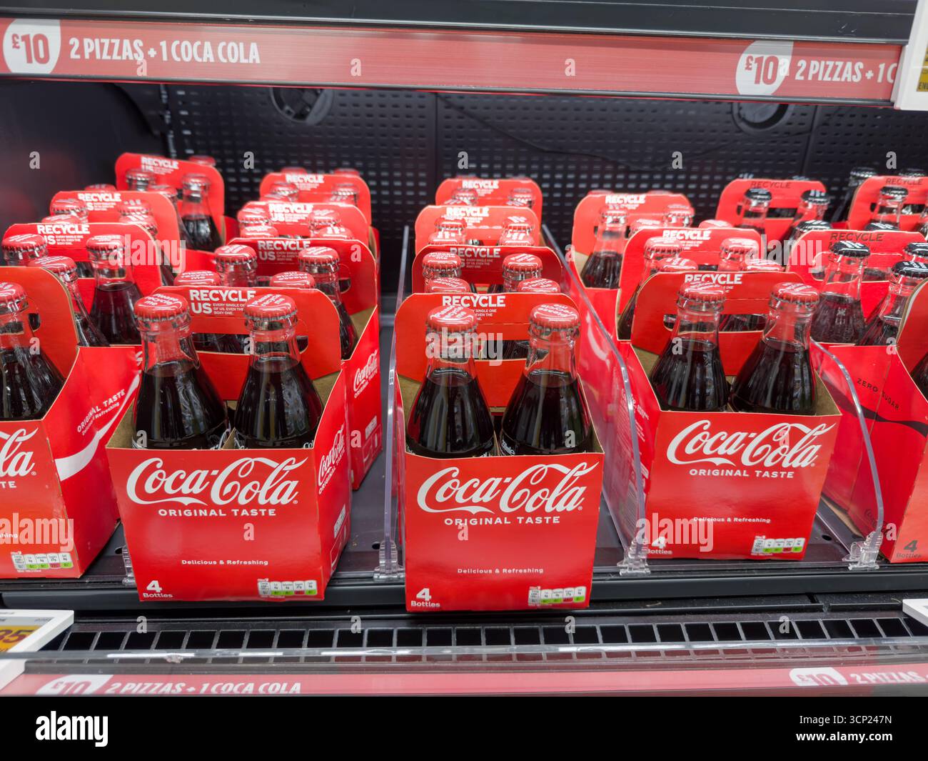 Diverse confezioni Coca-Cola da quattro bottiglie in cartone rosso sono disposte su un ripiano refrigerato per la vendita all'interno di un negozio Amazon Fresh di Londra. Foto Stock