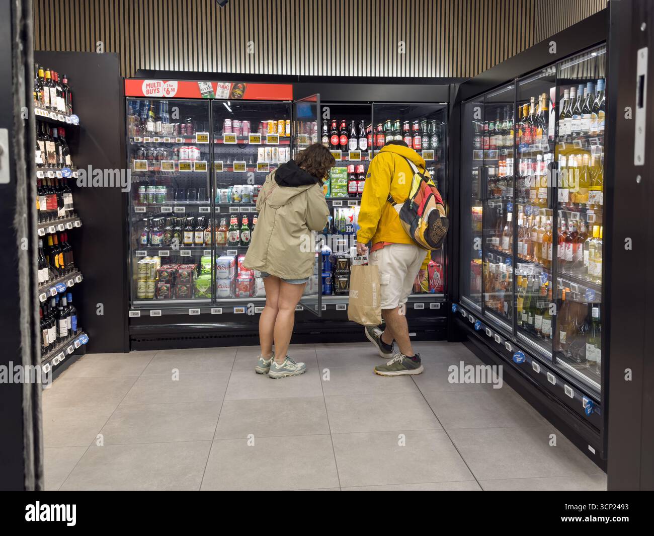 Un uomo e una donna che fanno acquisti curiosano e scelgono bevande alcoliche in una sezione dedicata agli oltre 25 clienti in un negozio Amazon Fresh a Londra. Foto Stock