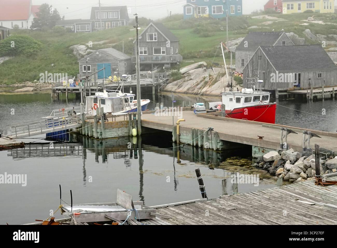 Una vivace barca da pesca rossa è attraccata nel tranquillo porto di Peggy's Cove, nuova Scozia. Intorno all'area ci sono edifici rustici in legno e una casa accogliente Foto Stock