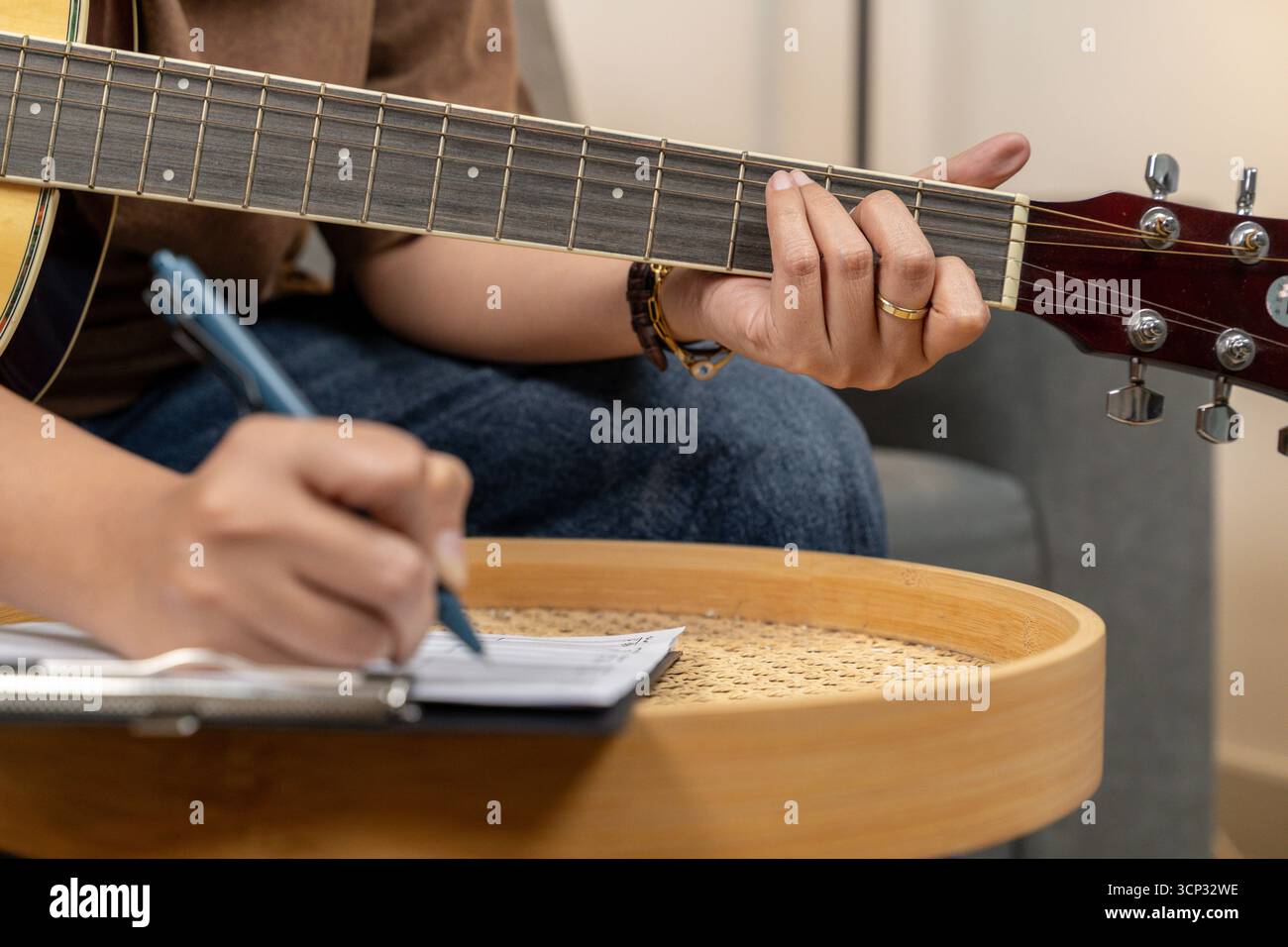la giovane donna creativa si sta divertendo con il suo hobby, suonando abilmente una chitarra mentre si concentra sulla scrittura di note musicali nel suo taccuino. La scena captur Foto Stock