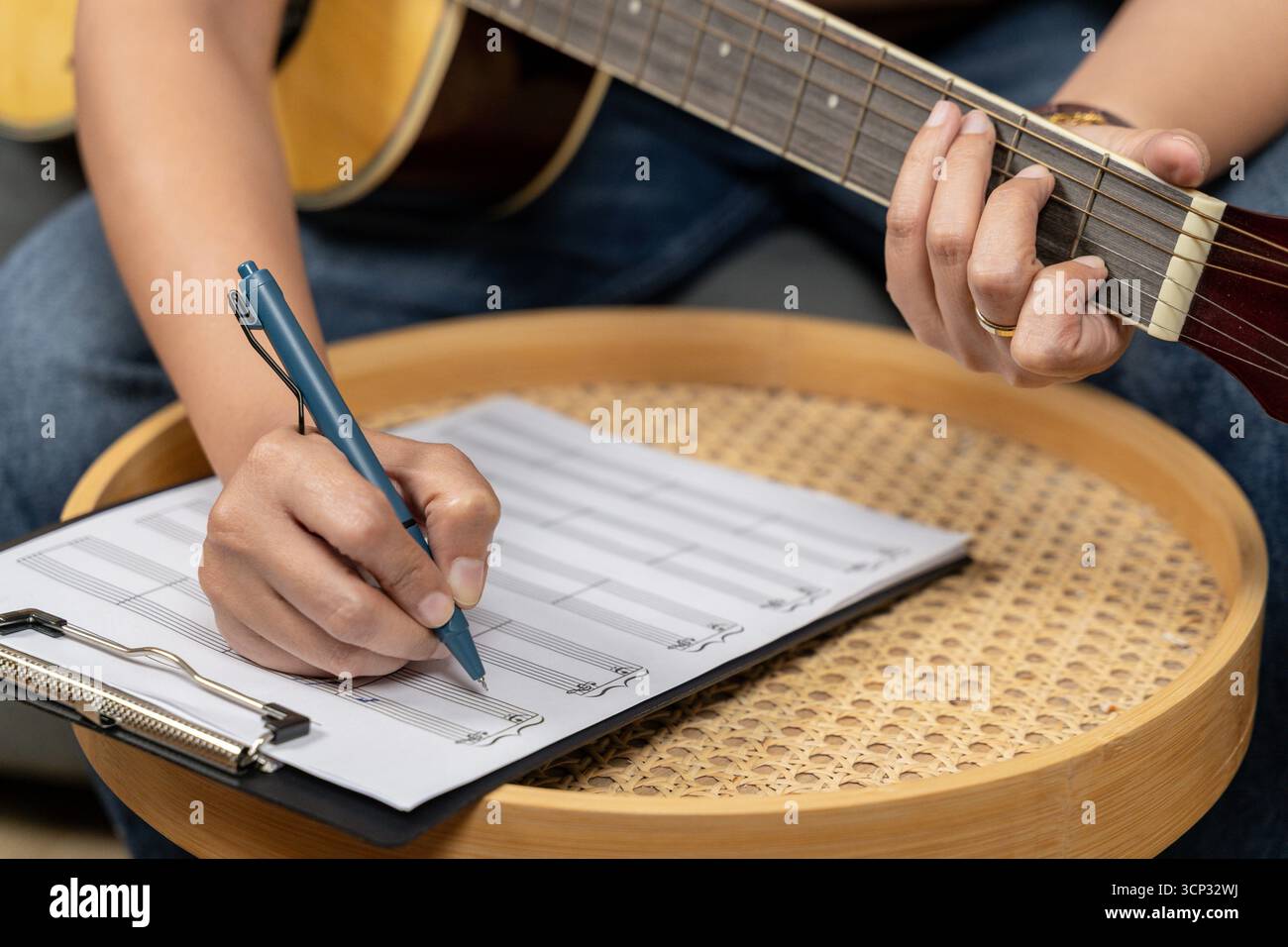 Una giovane donna creativa si sta divertendo con il suo hobby, suonando abilmente una chitarra mentre si concentra sulla scrittura di note musicali nel suo taccuino. La scena capt Foto Stock