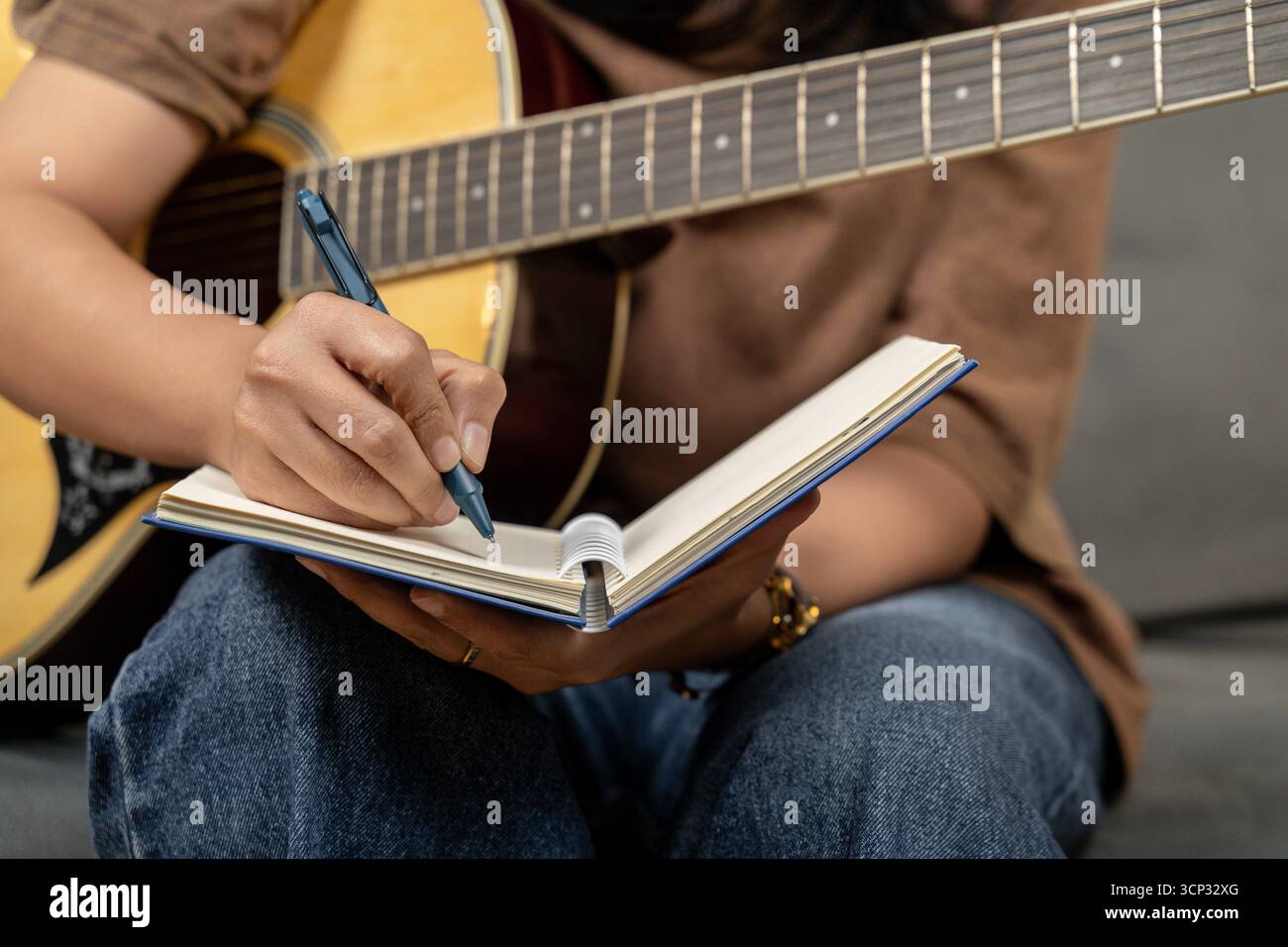 Una giovane donna creativa si sta divertendo con il suo hobby, suonando abilmente una chitarra mentre si concentra sulla scrittura di note musicali nel suo taccuino. La scena capt Foto Stock