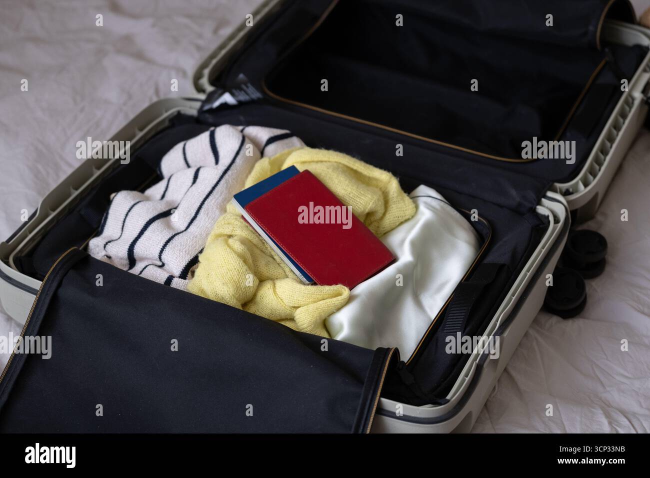 Valigia aperta con gli indispensabili da viaggio, tra cui maglieria, indumenti in seta, passaporto e checklist scritta a mano. Una rappresentazione accogliente e realistica del pacchetto Foto Stock