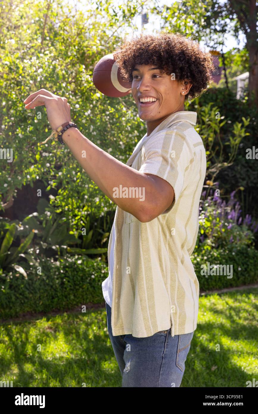 Uomo afroamericano che lancia football nel giardino del cortile con braccialetti Foto Stock