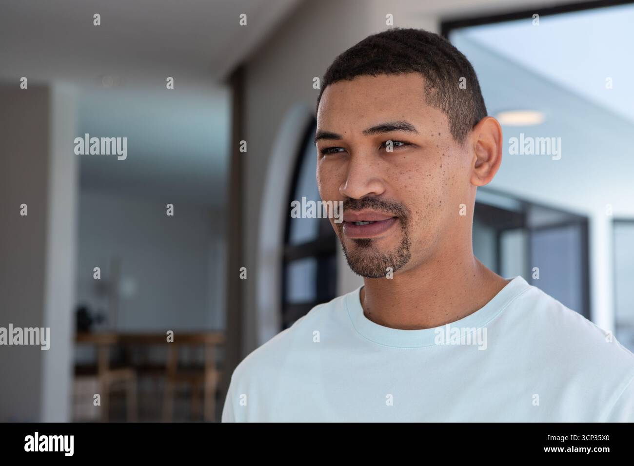Uomo afro-americano che posa nel soggiorno indossando una maglietta bianca vicino al tavolo da pranzo sedie spazio fotocopie Foto Stock