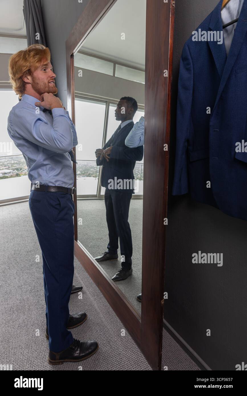 Diversi colleghi di sesso maschile adattano l'abbigliamento formale nella suite dell'hotel con specchio e giacca Foto Stock