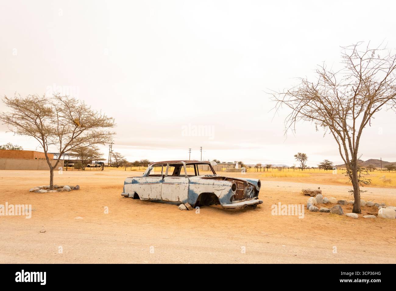 Il cimitero automobilistico di Solitario in Namibia presenta auto d'epoca arrugginite vicino a piccoli edifici desertici, adagiate contro dune e montagne, catturando il fascino del deserto Foto Stock