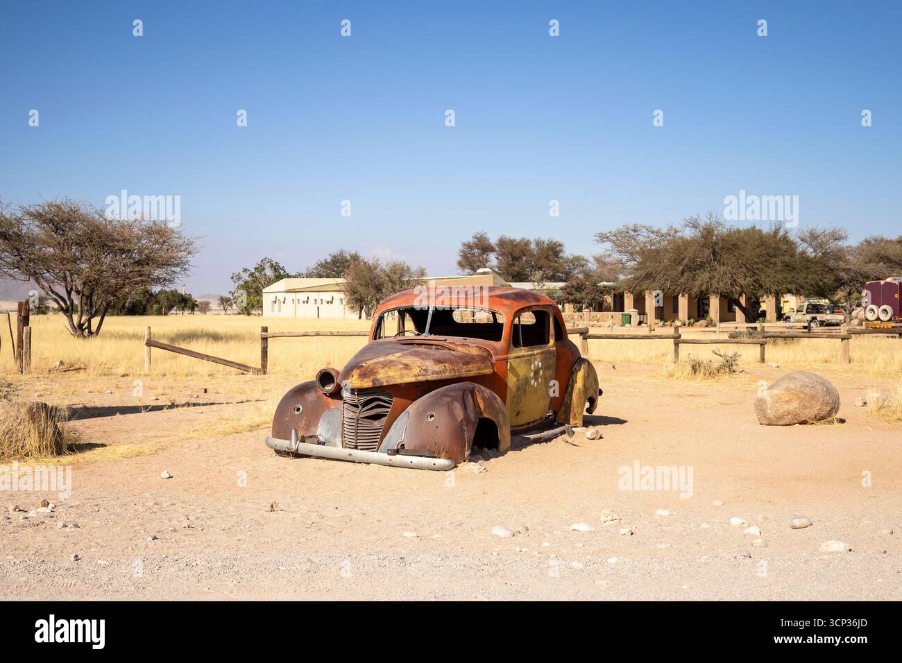 Il cimitero automobilistico di Solitario in Namibia presenta auto d'epoca arrugginite vicino a piccoli edifici desertici, adagiate contro dune e montagne, catturando il fascino del deserto Foto Stock
