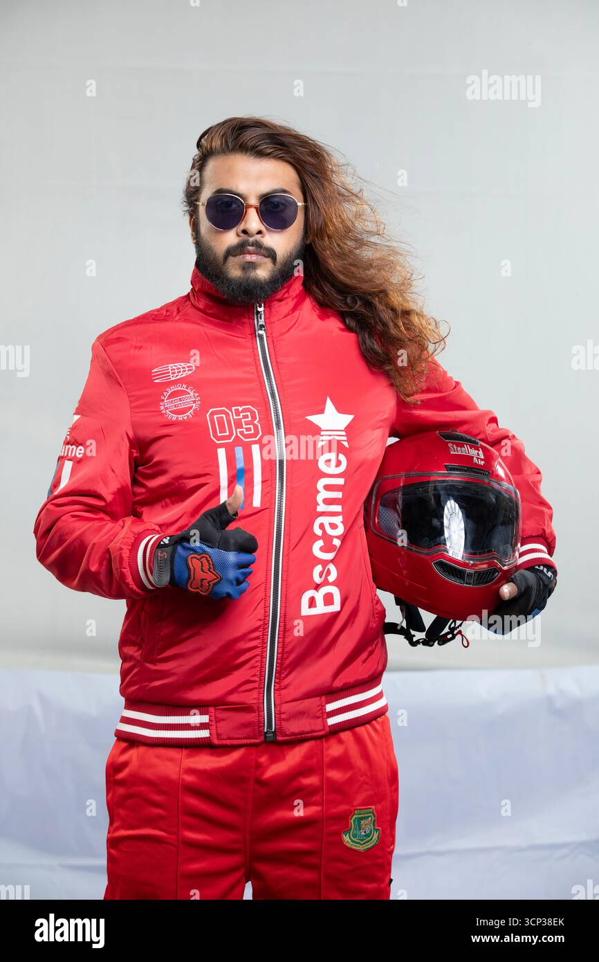 Uomo con capelli lunghi e occhiali da sole in una giacca rossa con casco da moto Foto Stock