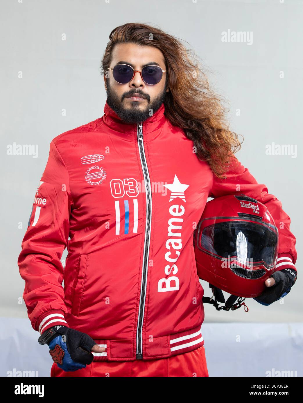 Uomo con capelli lunghi e occhiali da sole in una giacca rossa con casco da moto Foto Stock