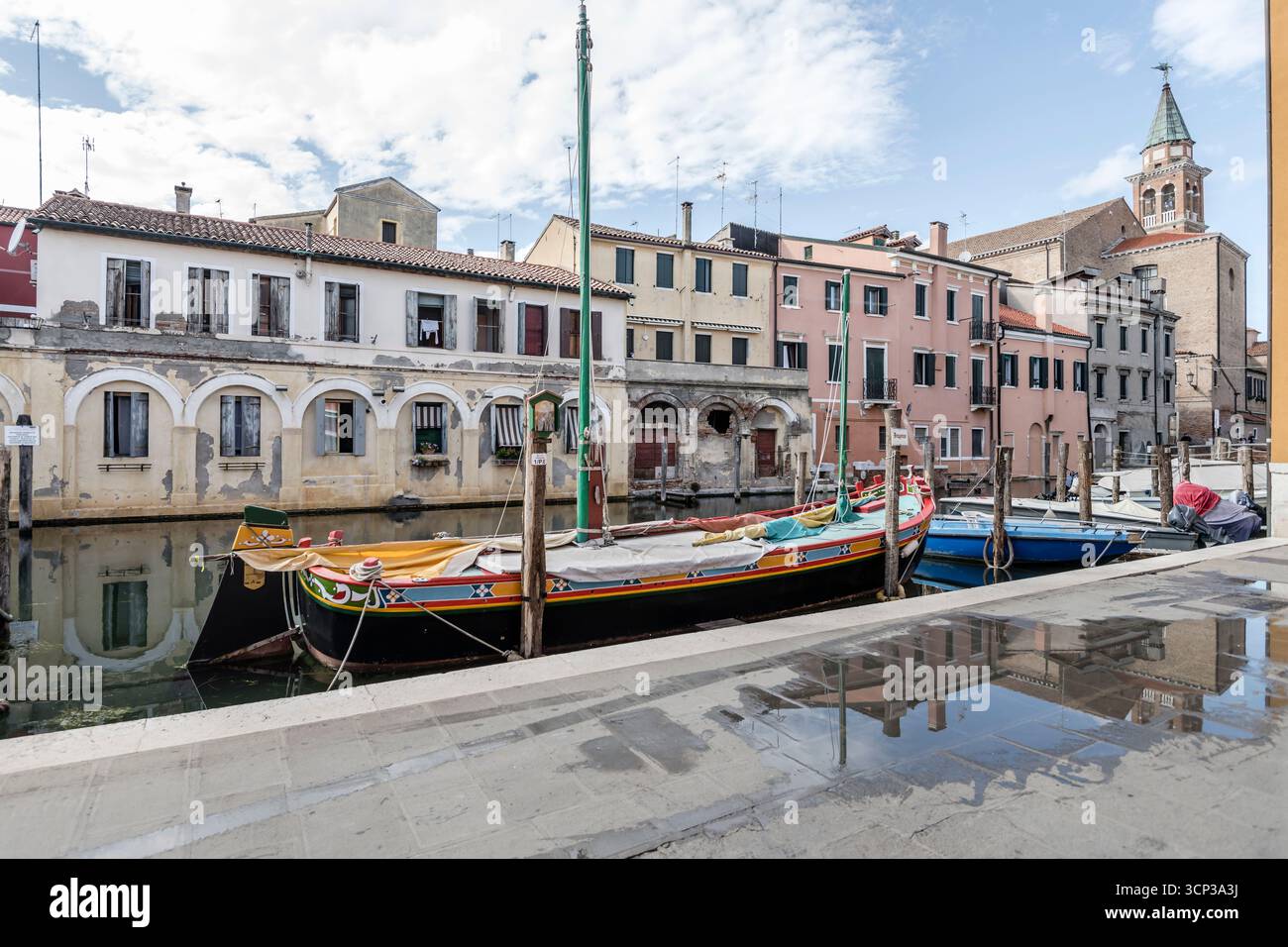 Paesaggio urbano con passeggiata in pietra sulla riva del canale Vena, girato alla luce estiva a Chioggia, Veneto, Italia Foto Stock