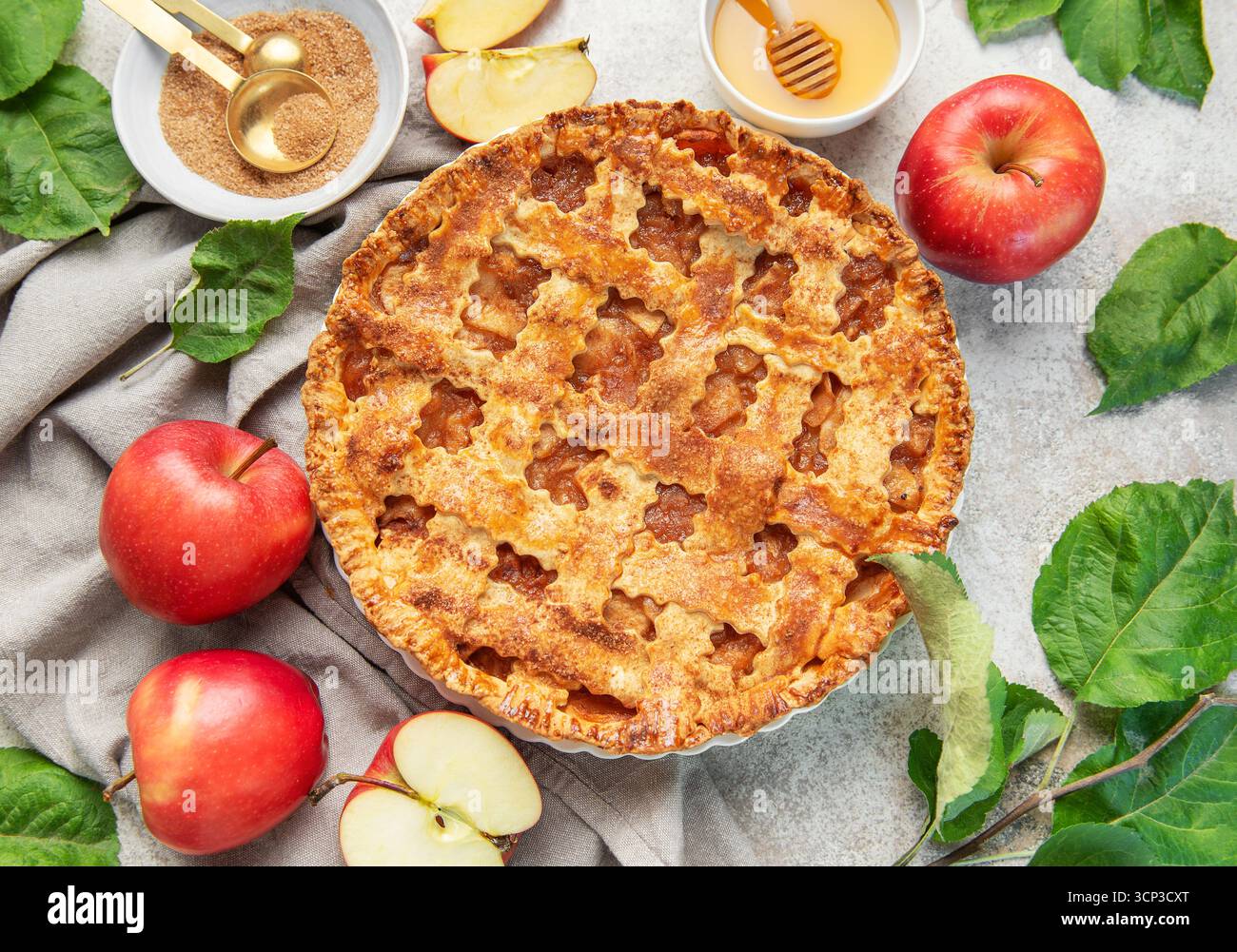 Classica torta di mele circondata da mele fresche, miele, zucchero di canna e decorata con foglie di mele Foto Stock