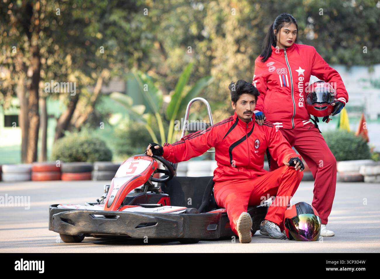 Uomo e donna in tute rosse in posa con un go-kart su una pista da corsa Foto Stock