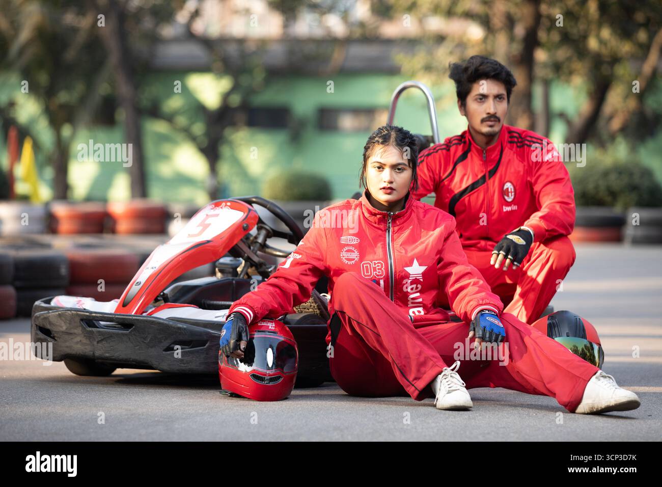 Uomo e donna in tute rosse in posa con un go-kart su una pista da corsa Foto Stock