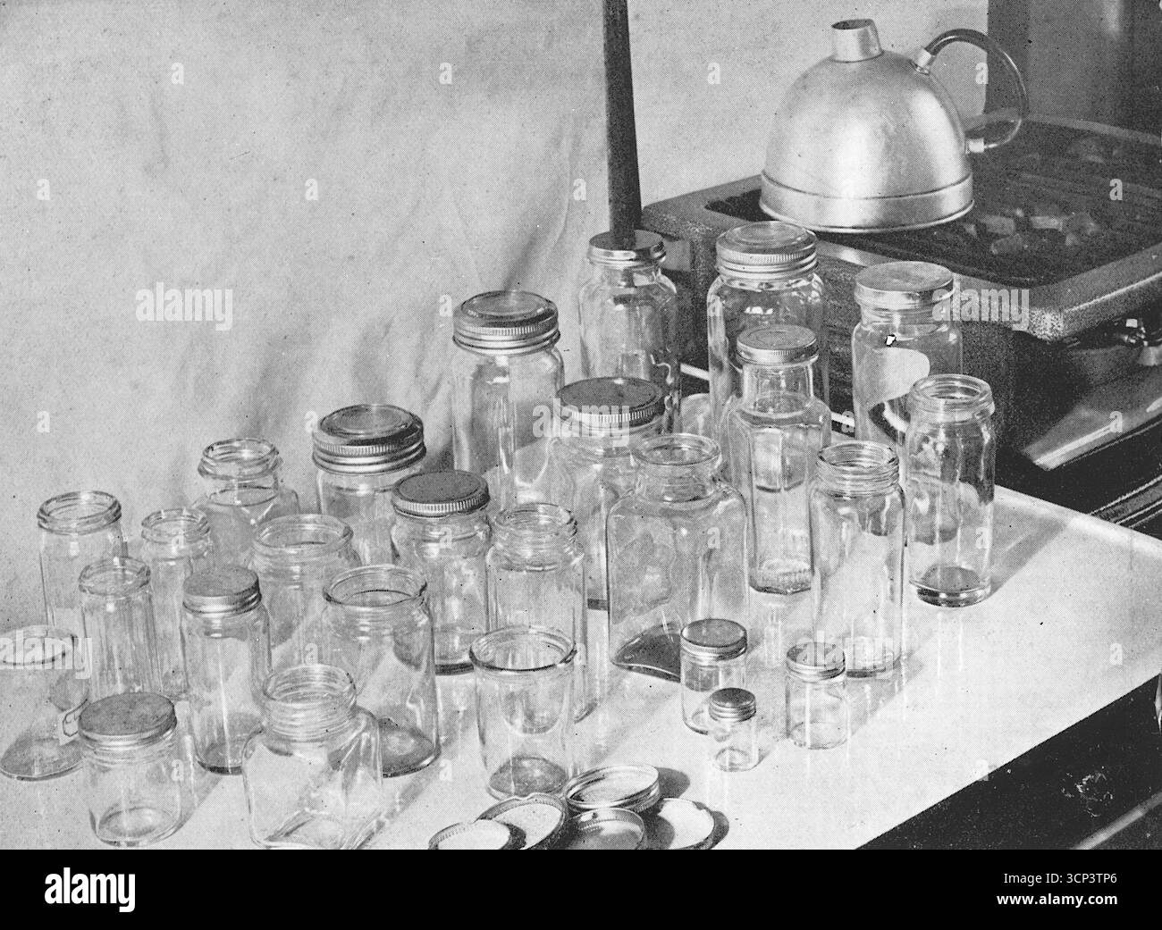 Un ampio display di vasetti in vetro degli anni '1930 utilizzati nella produzione di marmellate, su un piano di lavoro in smalto. Da una fotografia stampata che originariamente apparve nella pubblicazione, The Vulcan Cook Book, che fu pubblicato nel 1936 dalla Vulcan Stove Company di Exeter, Inghilterra. Foto Stock