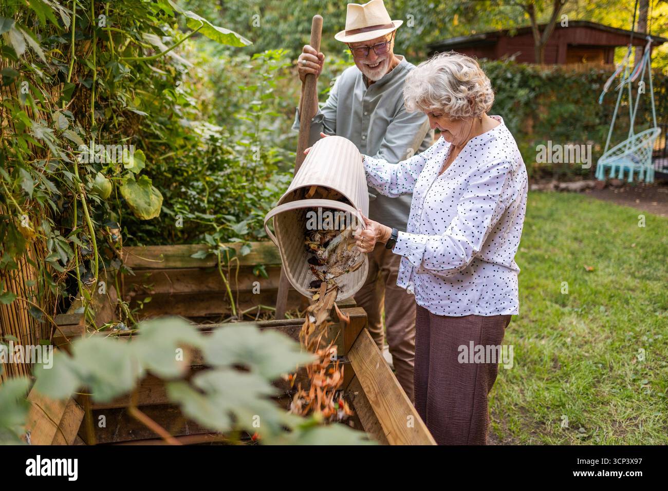 Una coppia anziana che lancia rottami di verdure in un cumulo di compost nel giardino Foto Stock