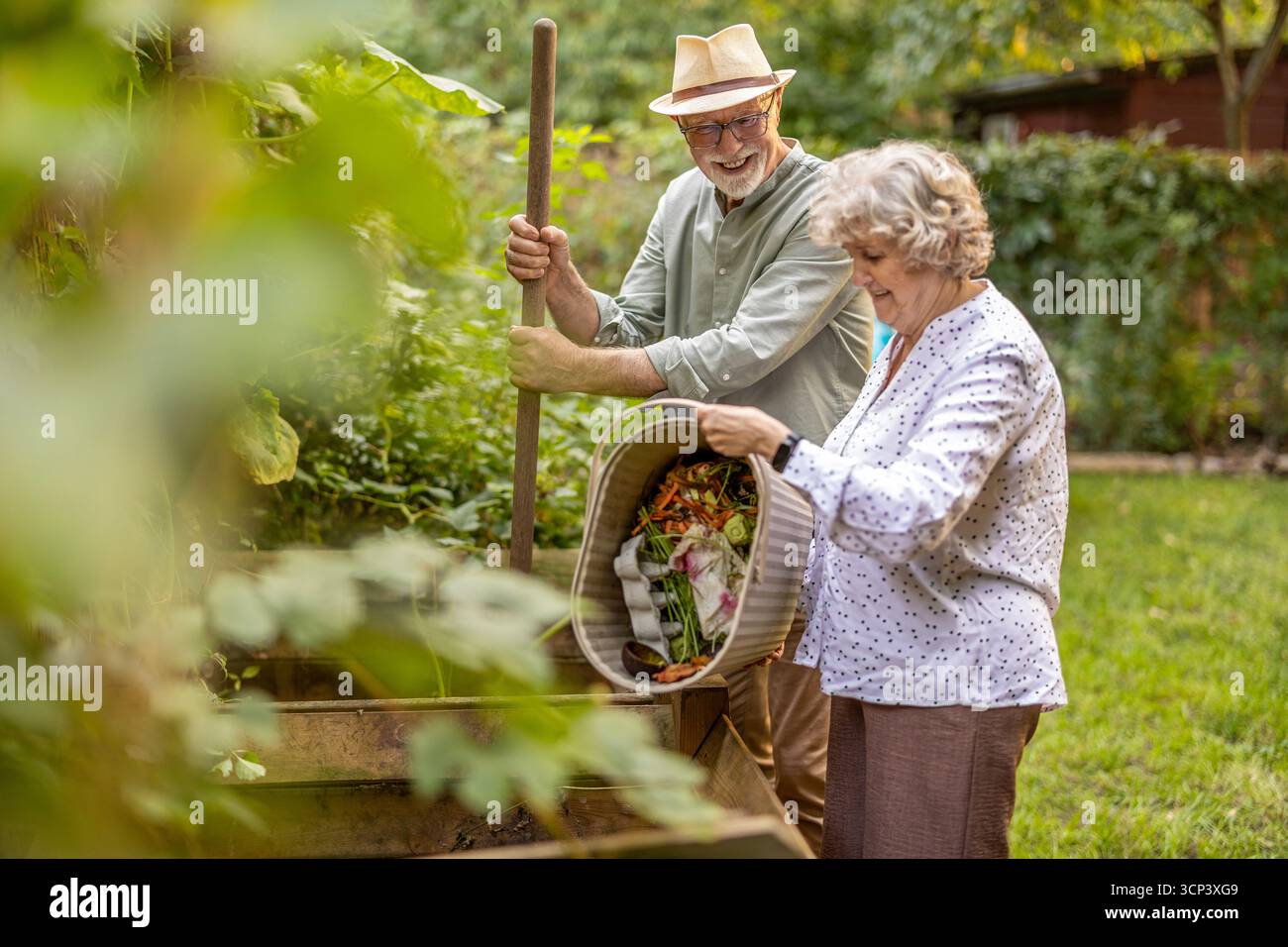 Una coppia anziana che lancia rottami di verdure in un cumulo di compost nel giardino Foto Stock