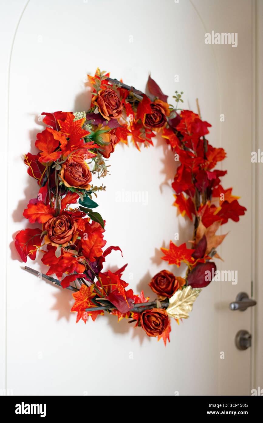 L'autunno arancione scuro lascia una corona decorativa stagionale su una porta bianca Foto Stock