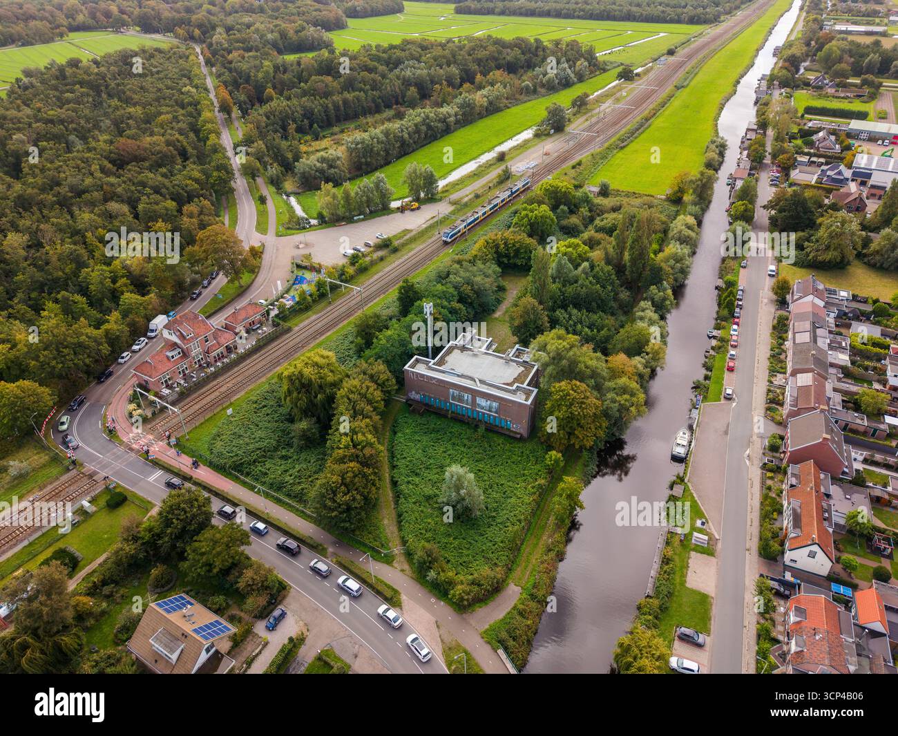 Vista aerea di un'area semi-rurale con ferrovia, stazione ferroviaria, canale con barche, edificio con tetto solare, case con tetto rosso, fusione di foreste e campi Foto Stock