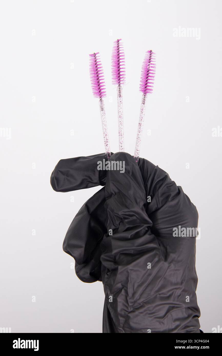 La mano di una makeup artist tiene le ciglia e le sopracciglia rosa Foto Stock